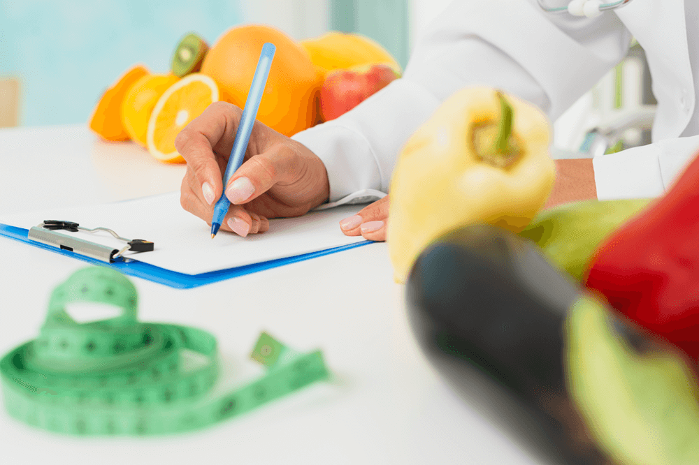 Nutritionist writing a personalised health plan with fresh fruits, vegetables, and measuring tape on desk
