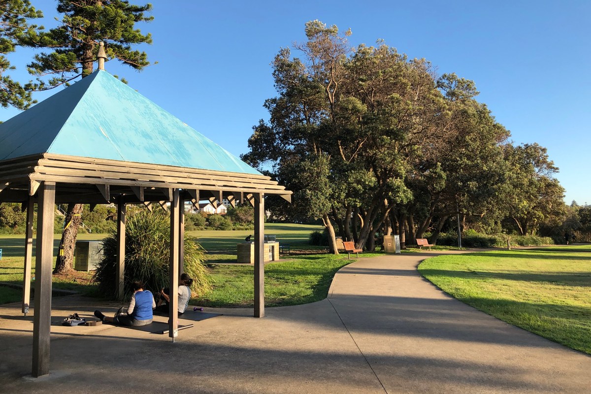 Park path and gazebo with people on exercise mats Park path and gazebo on a sunny morning, with two people sitting on exercise mats in the shade