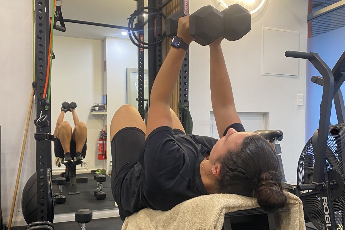 Client doing a dumbbell chest press on a bench with a fan running at The Fitness Space studio in Maroubra Client doing a dumbbell chest press on a towel-covered bench with a fan running at The Fitness Space studio in Maroubra